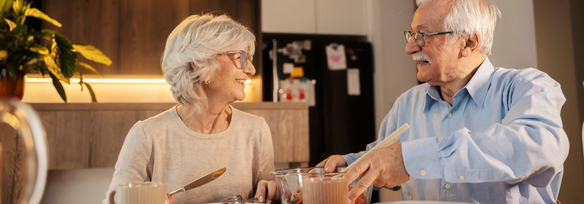 Małżeństwo seniorów uśmiecha się patrząc na siebie przy posiłku